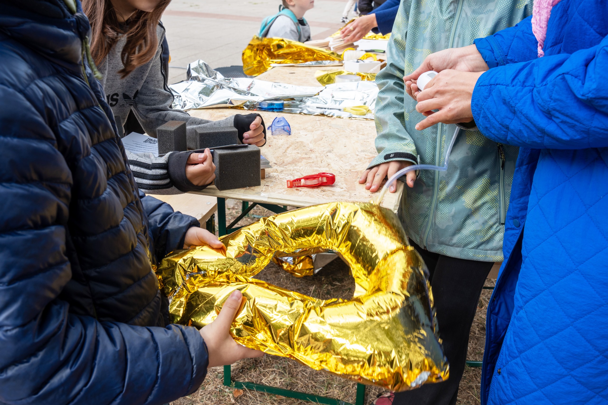 Workshopsituation, bei der Kinder und Jugendliche aufblasbare Strukturen aus goldenen Notfalldecken bauen