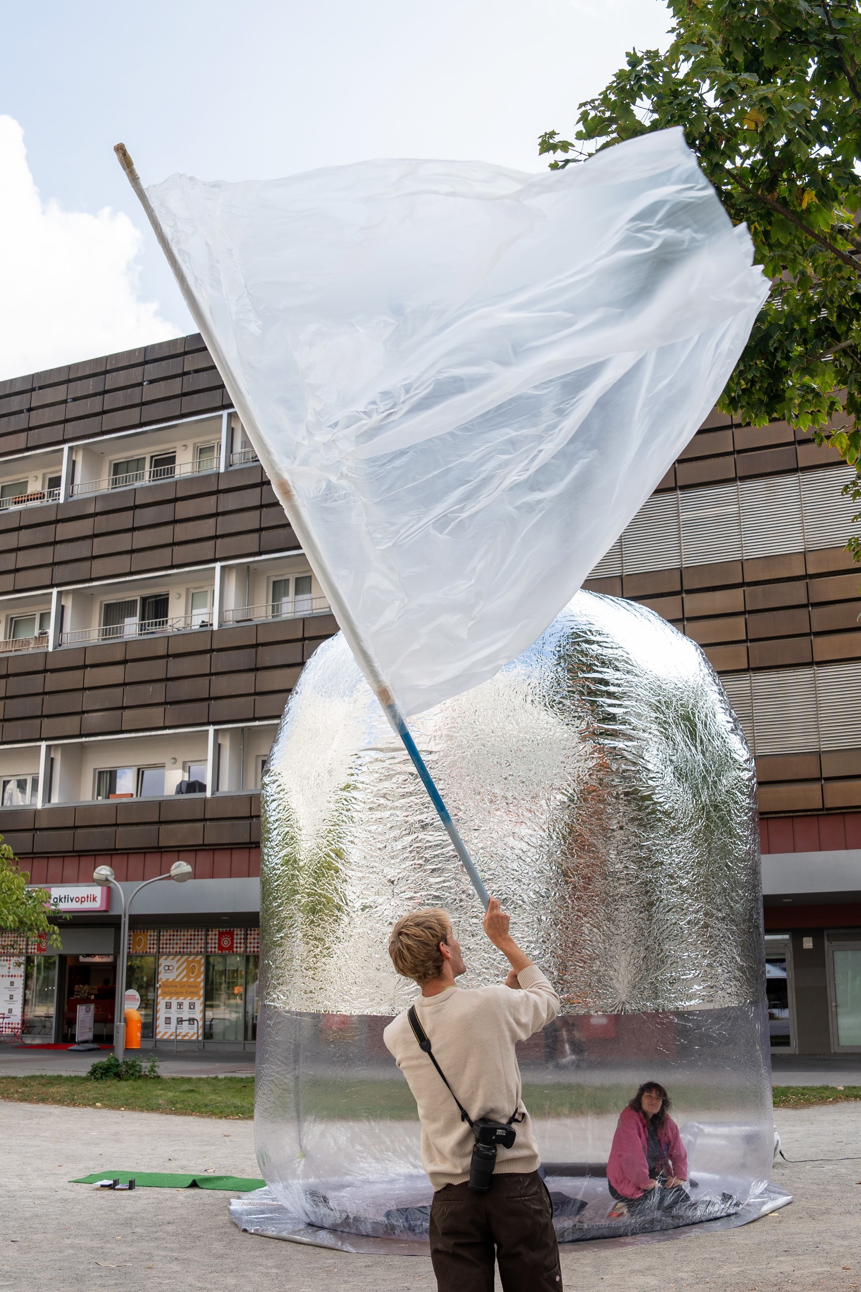 Aufblasbare Installation von Popticum mit unterem transparenten und oben silbernen Teil. Davor eine Person mit transparenter Flagge
